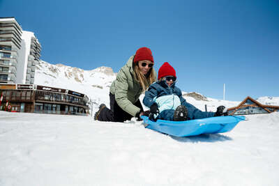 Kind auf einem Schlitten mit seiner Mutter in Tignes